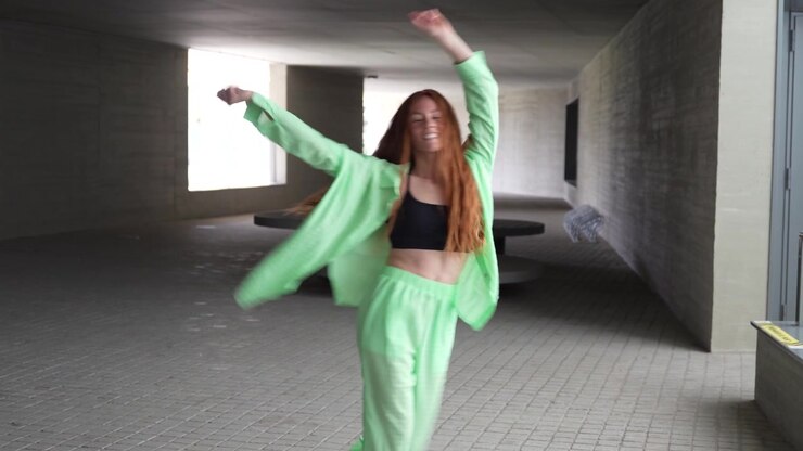 A woman dressed in green is happily dancing in a modern city environment exuding energy and joy