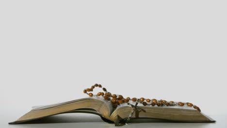 rosary beads falling onto open bible on white background