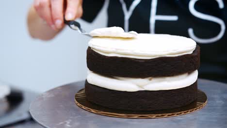 close up of baker spreading buttercream on chocolate cake