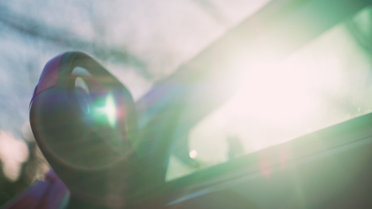 Bellissimo flare anamorfico del sole che filtra attraverso il parabrezza di un'auto mentre la telecamera si muove oltre lo specchietto retrovisore laterale