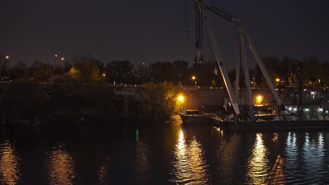 View from boat sailing at night in the river along the city with beautiful reflections of city lights in water.