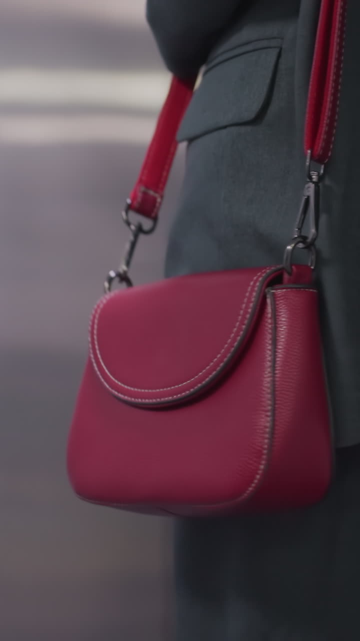 Close-up shot of red leather handbag carried by confident businesswoman in office attire. Stylish accessory complementing professional look in modern office environment, showing details of bag
