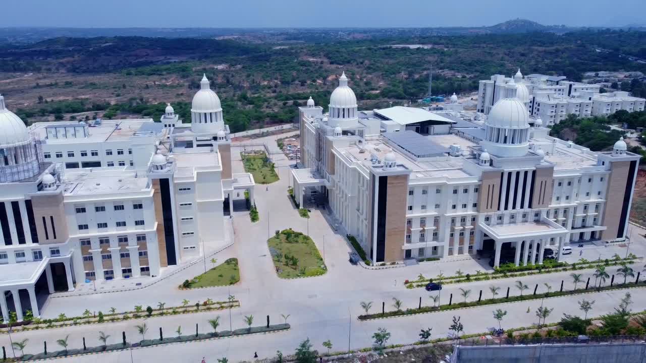 A wide aerial shot pulling back to reveal the massive scale of the Kanha Shanti Vanam campus in India, a grand complex of interconnected, neo-classical buildings set in a hilly landscape