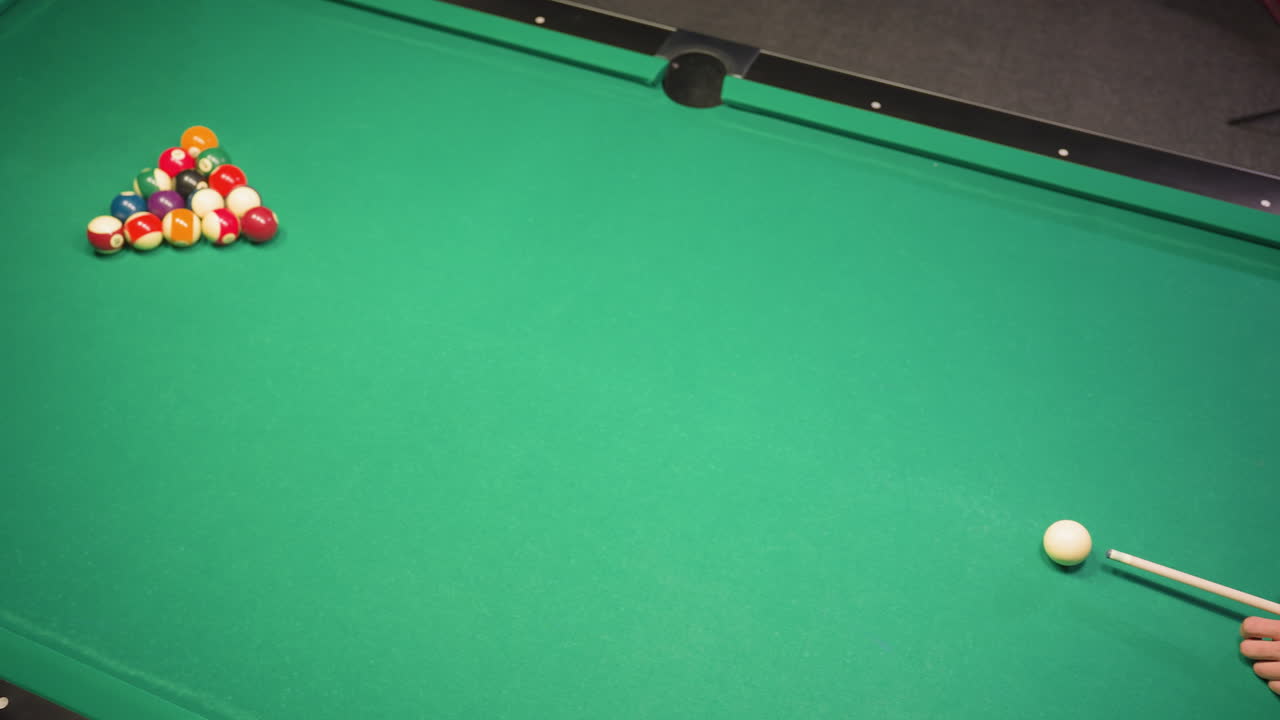 Player in white shirt grips cue stick, eyes locked on cue ball, preparing precise shot on green pool table. Focus, skill, and concentration evident in stance, showcasing intense gameplay anticipation