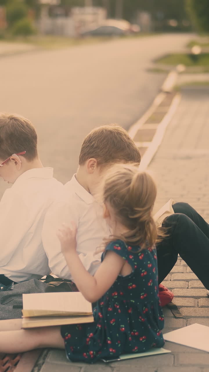 young lady with fair hair in ponytail talks and flirts with brothers sitting on grey road pavement against building