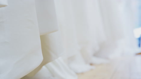 close up of beautiful bridal wedding dresses hanging on rail in shop