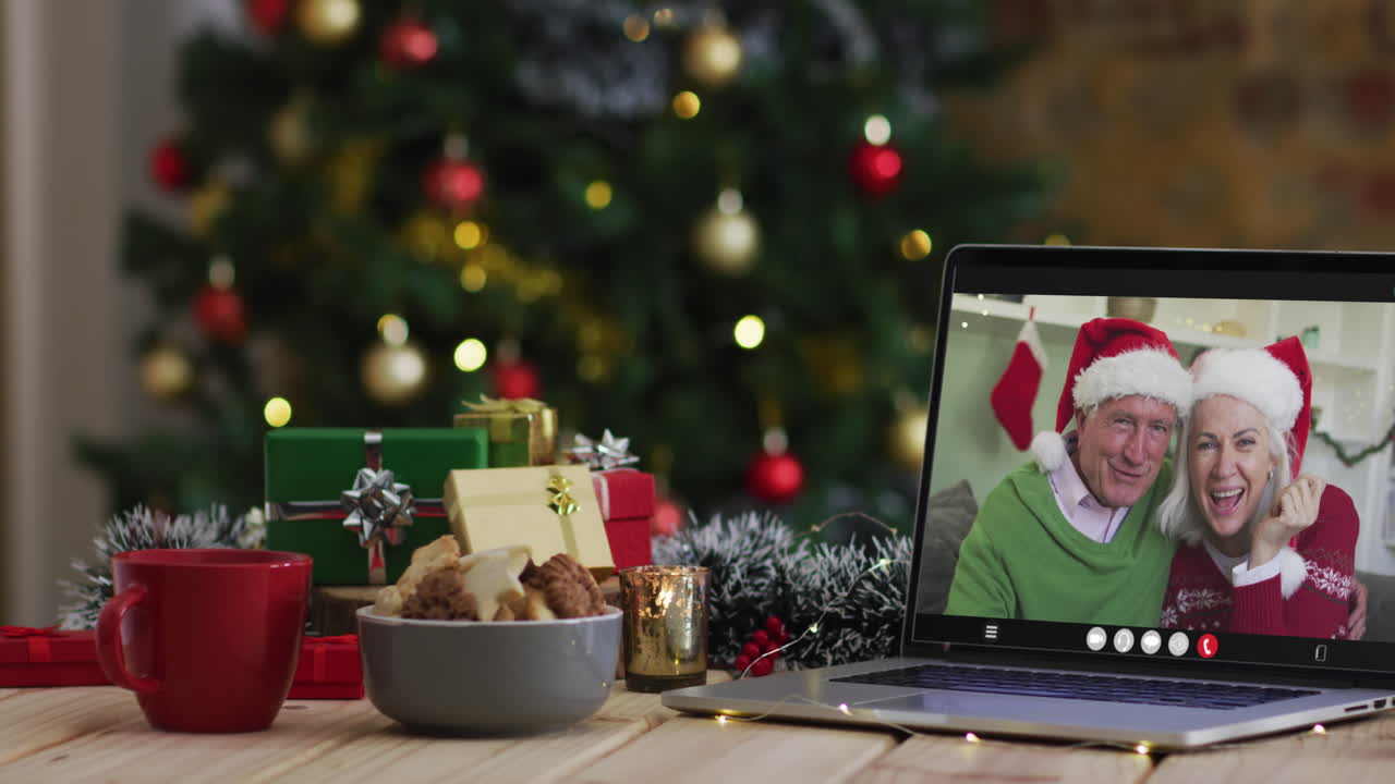 una pareja de alto nivel caucásica saludando en una videollamada en una computadora portátil, con un árbol de navidad