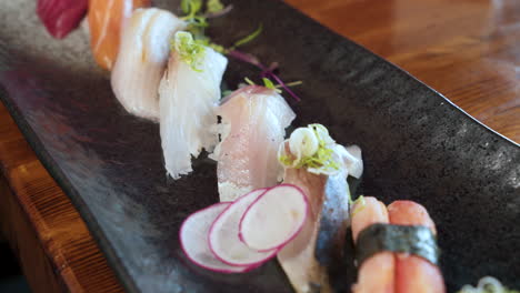 chopsticks pick up a piece of sushi from colorful platter of traditional nigiri in japanese restaurant, slider close up 4k