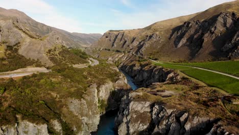 Beautiful-view-of-rocky-river-canyon,-rock-formations-and-vineyard,-New-Zealand---aerial