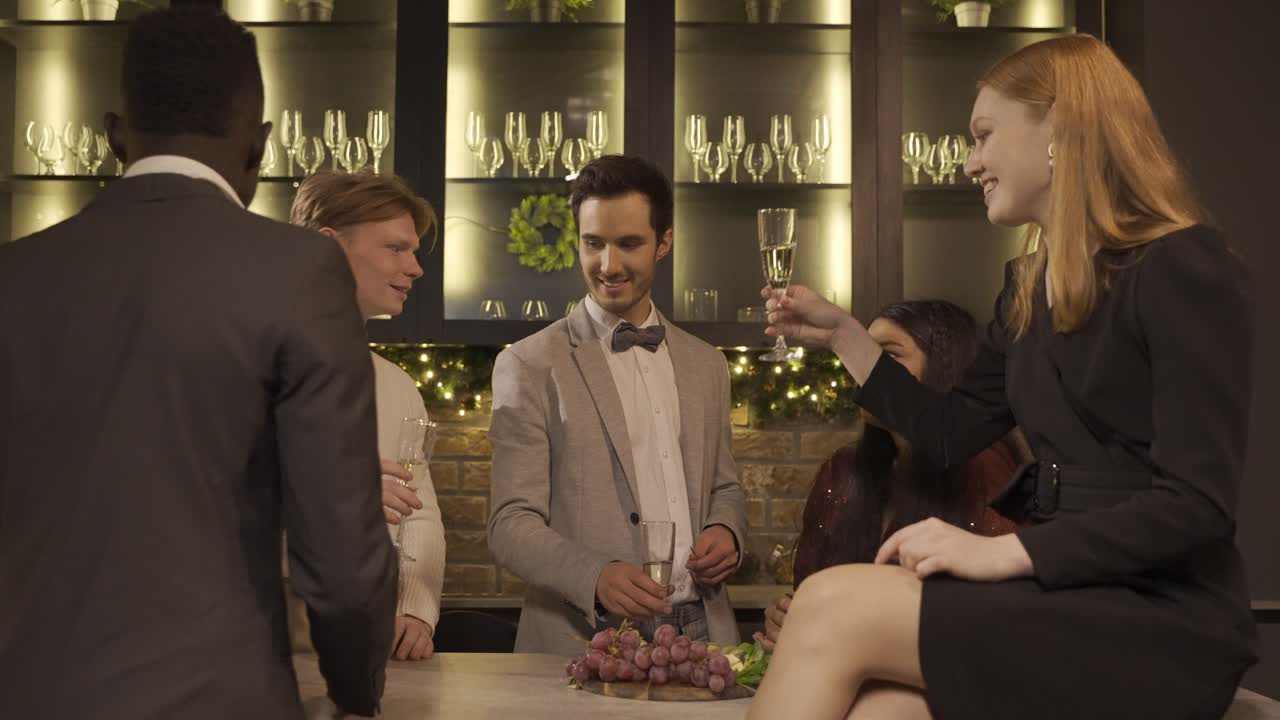 Group of friends dressed in elegant clothes celebrating the New year's party, they stand around the bar counter while toasting and drinking champagne