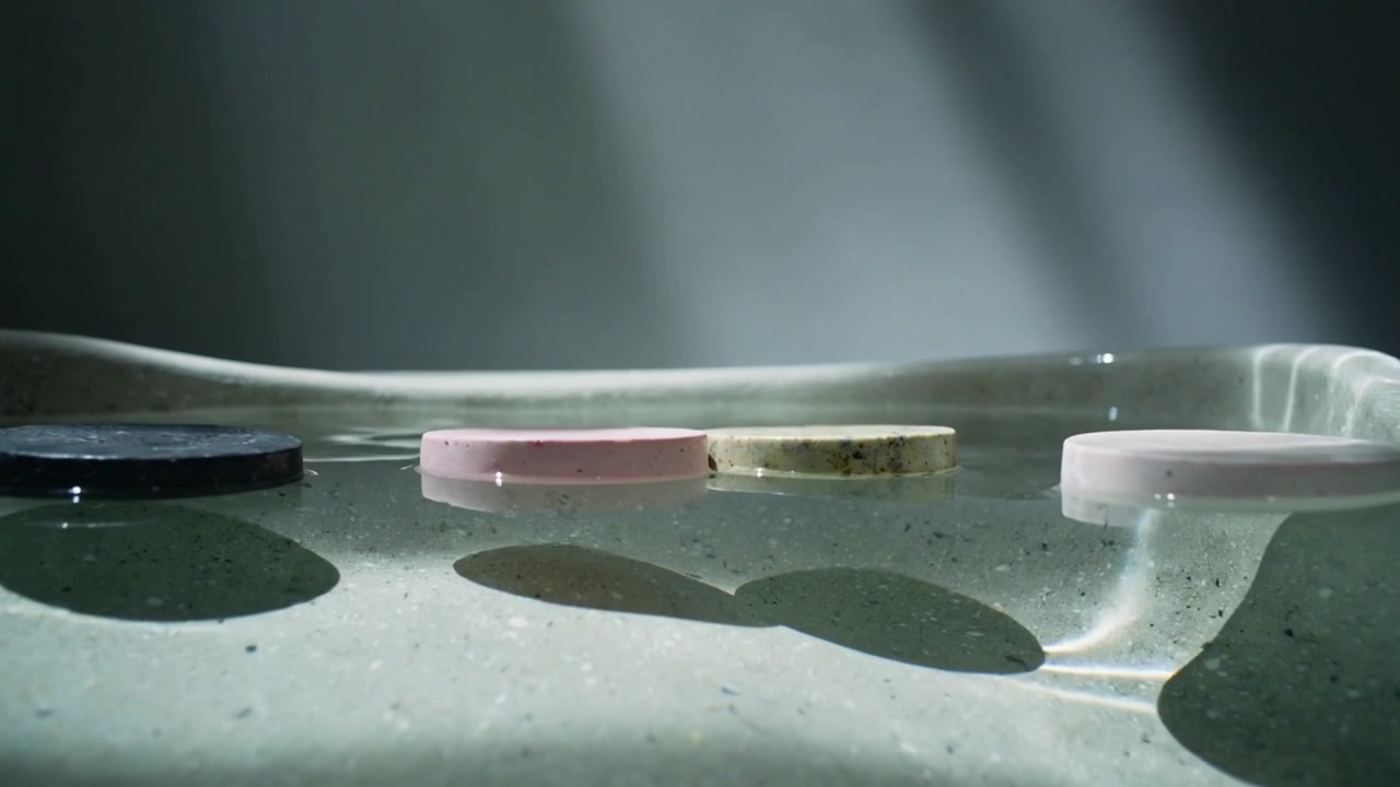 Bobbing three puck-like objects drifting on studio basin water, following gentle waves and light