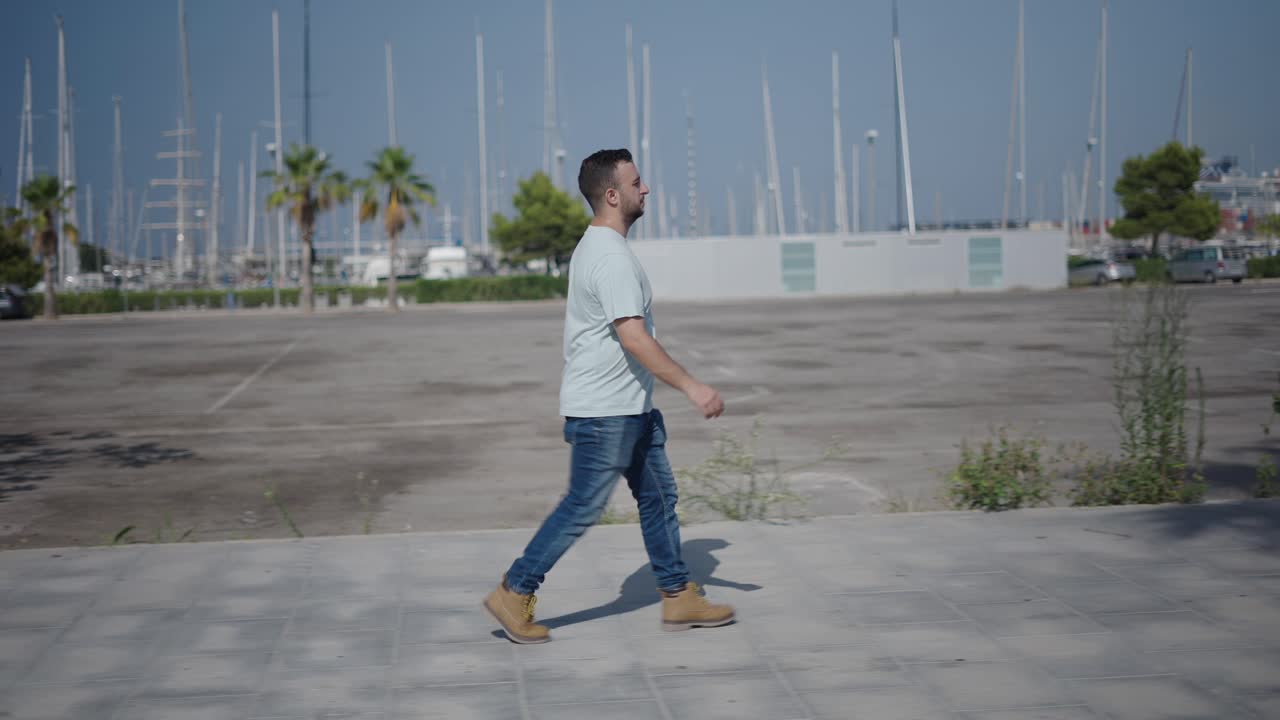 Man walking in a city parking lot near a marina on a sunny day