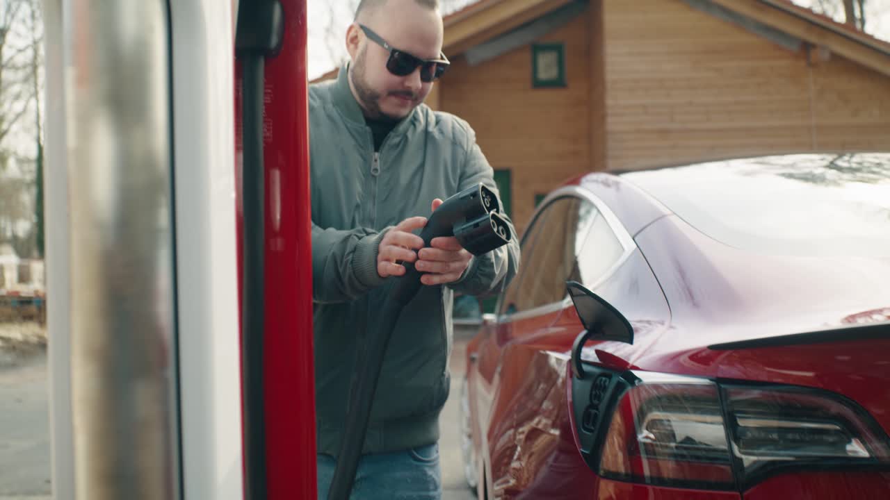 Man walks to the electric car, opens the charge port flap and plugs the charging cable