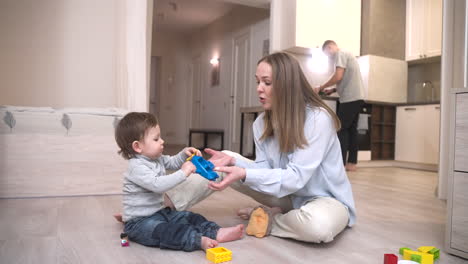 baby playing sitting on the floor with toys and with his mother