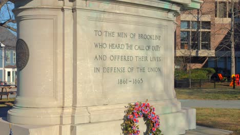 Corona-De-Flores-Y-Banderas-Americanas-De-Punta-De-Lanza-En-El-Suelo-Del-Monumento-De-La-Guerra-Civil-Con-Estatua-Ecuestre-En-Pedestal-En-Brookline,-Massachusetts