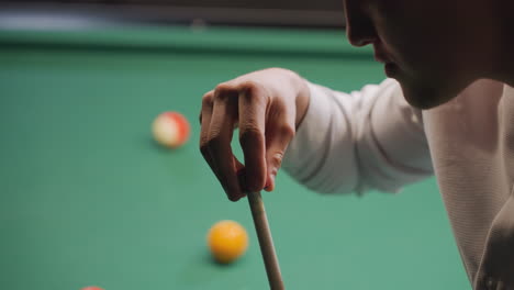 young man in white shirt chalking cue stick before taking shot on green pool table. close-up highlights focus, precision, and preparation, with billiard balls visible in background