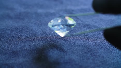 un joyero examinando un gran diamante translúcido usando pinzas de plata y guantes de látex negro para verificar si es auténtico o falso