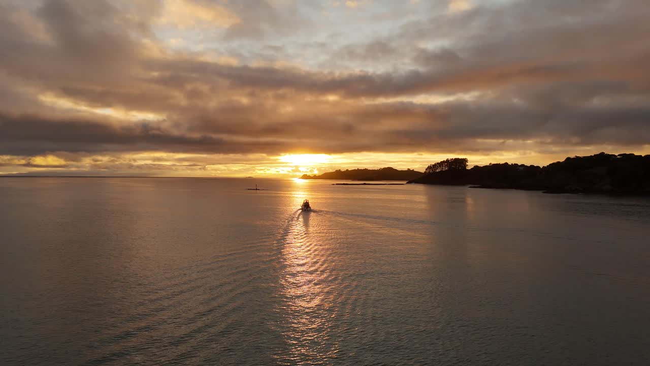 Barca che naviga sulle acque della Nuova Zelanda durante uno spettacolare tramonto dorato. Ampia ripresa aerea. Costa dell'area di Oneroa, isola di Waiheke