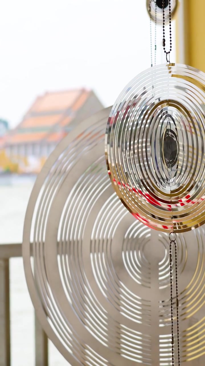 Et vindspil drejer blidt mod en baggrund af Bangkoks flodbred, der fanger refleksioner og bevægelse i skarpt dagslys.