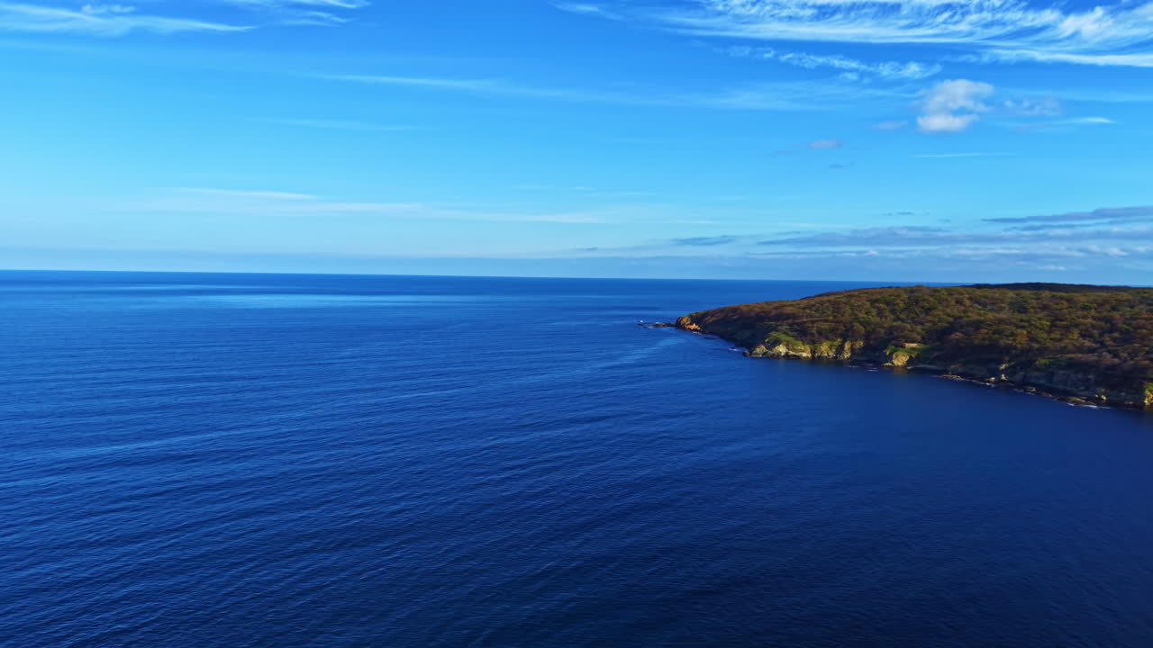 Una vasta distesa oceanica si estende verso l'orizzonte sotto un cielo blu brillante con nuvole leggere che la attraversano.