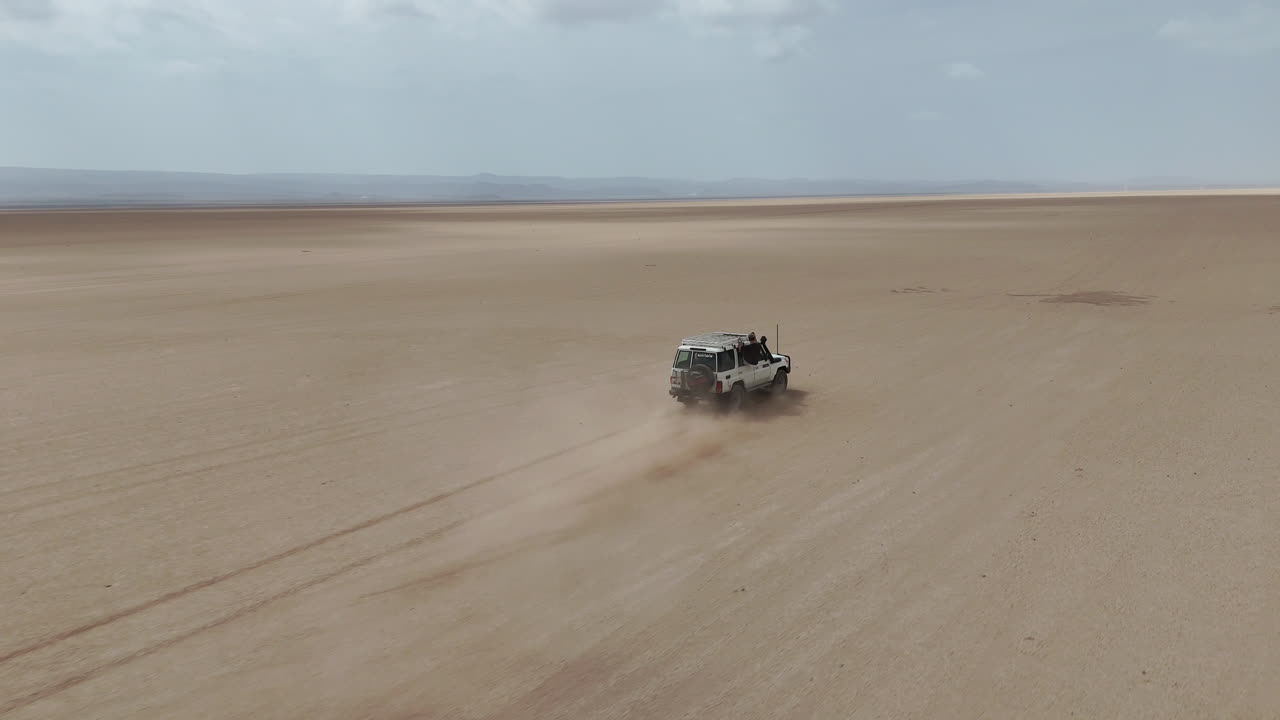 Ripresa cinematografica con drone di un veicolo che esplora un terreno arido con un lungo orizzonte desertico. Gibuti, Africa.