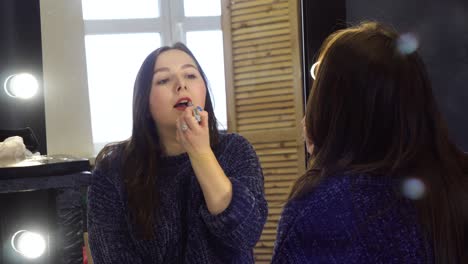 mujer aplicando lápiz labial frente a un espejo
