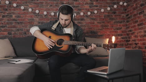 joven músico masculino creando, tocando guitarra y usando laptop en casa