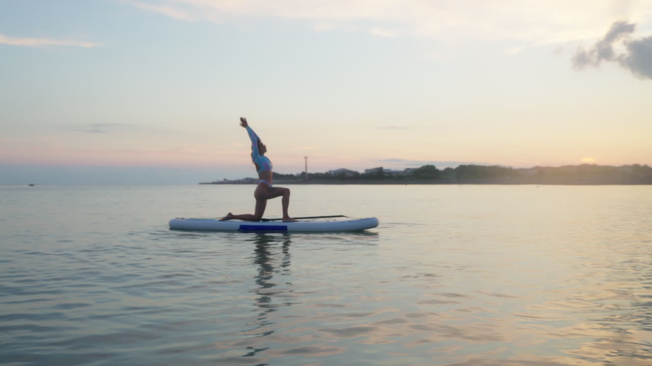 Woman practicing yoga on a stand-up paddleboard at sunset