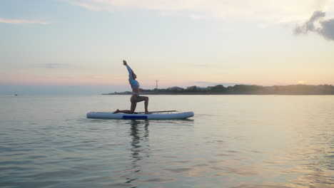 mujer practicando yoga en un paddleboard de pie al atardecer