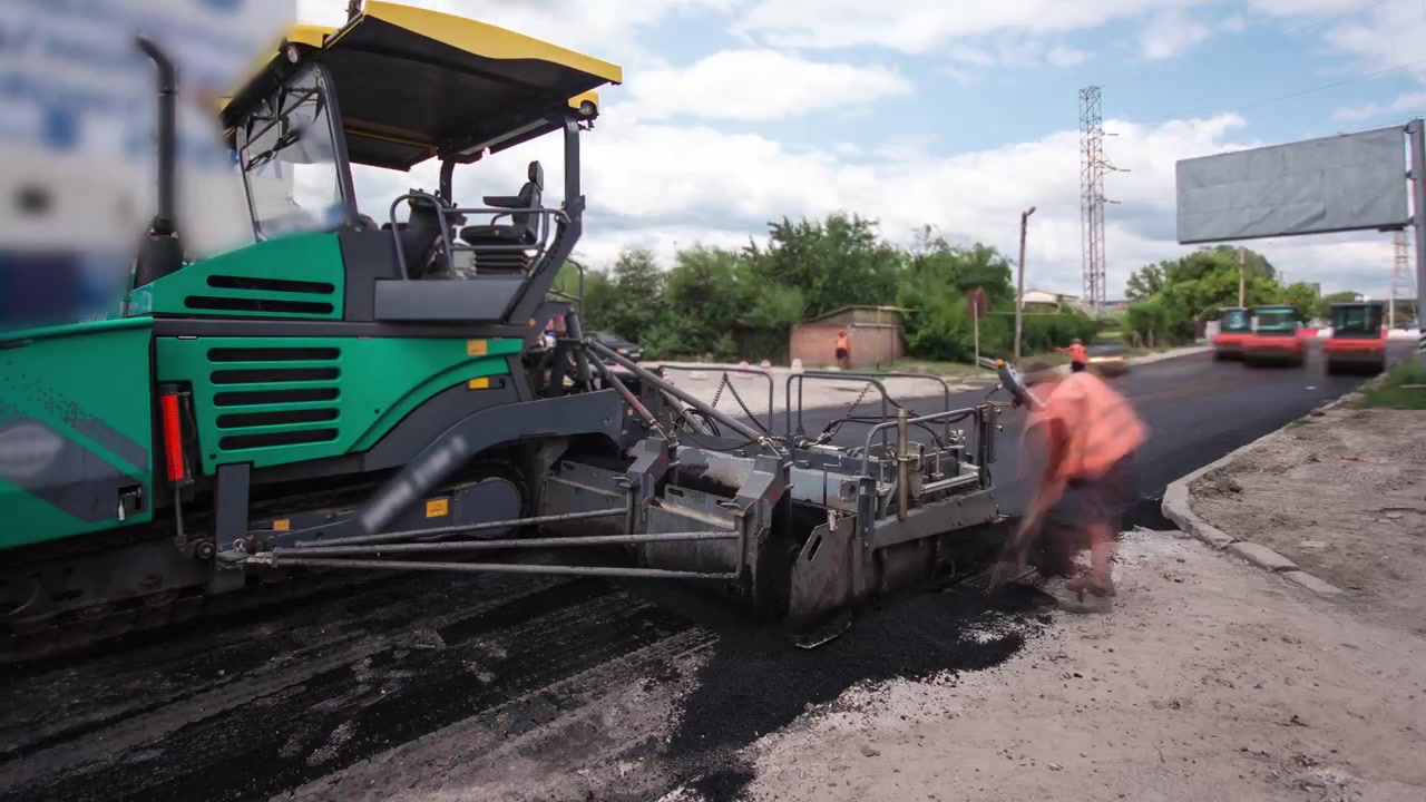 Una finitrice, finitrice per asfalto o macchina pavimentatrice che stende uno strato di asfalto durante un progetto di riasfaltatura timelapse. Camion con asfalto