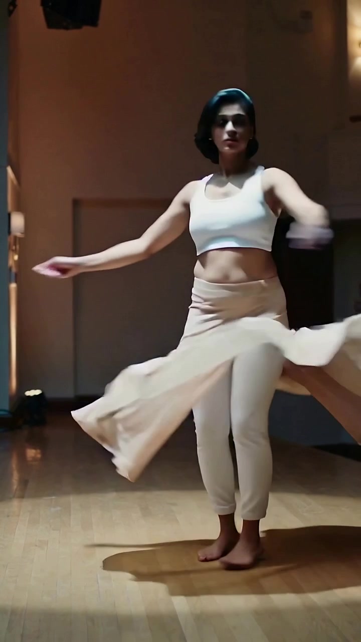 Vertikal video: Danser snurrer rundt og øver efter spotlight-signal på scenegulvet, iført vid nederdel og crop top.