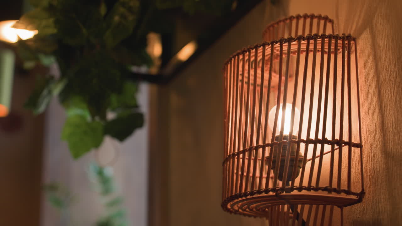 close up decorative wall light with wooden slats casting intricate shadows on textured wall beside lush vine leaves creating atmospheric contrast between warm glow