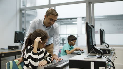 focused schoolgirl looking teacher typing on computer keyboard