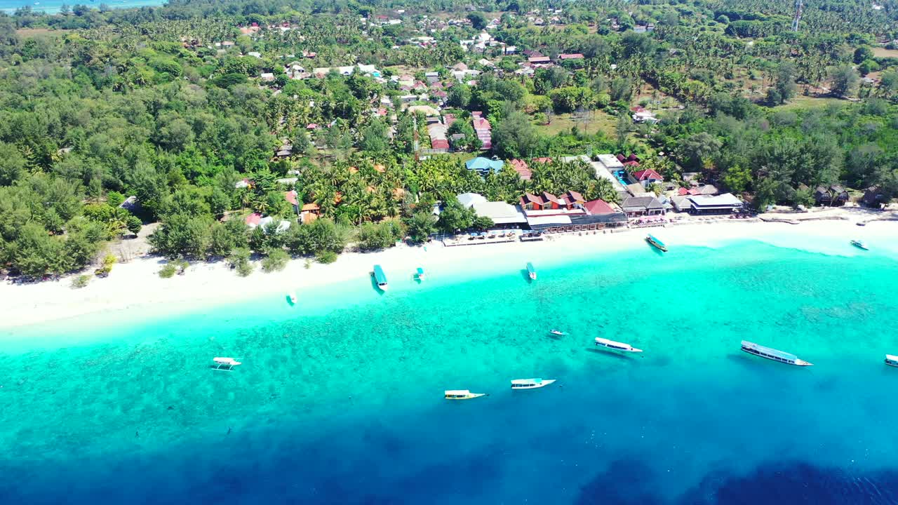 Spiaggia esotica idilliaca con sabbia bianca circondata da una laguna azzurra piena di barche ancorate in attesa di turisti alloggiati nei resort di un'isola tropicale a Bali.