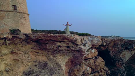 barefoot hippie girl practicing yoga at sunset near torre des carregador, ibiza, spain. speed ramp hyper motion time lapse. ascending drone
