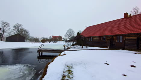 Dolly-forward-cinematic-view-of-Latvian-cottage-site-in-midwinter,-thaw-natural-pool-upfront