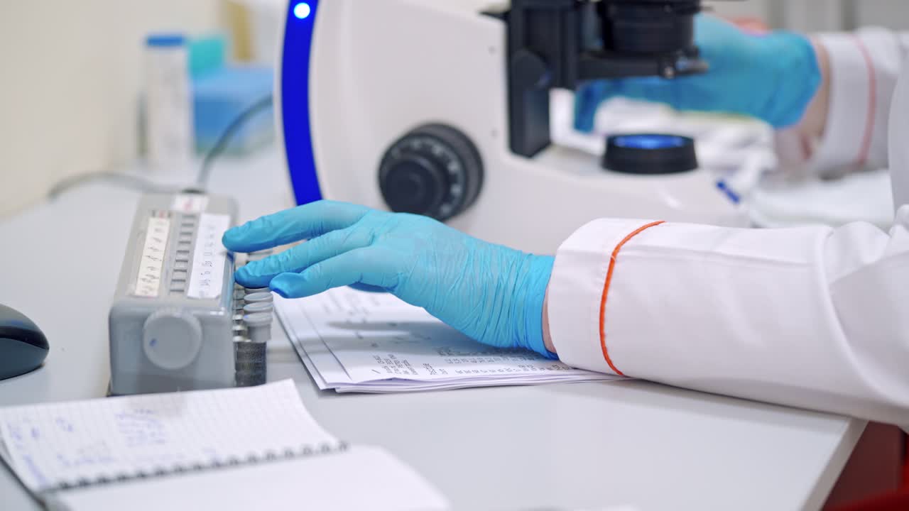 Hands in blue gloves of medical worker. Laboratory scientist works with microscope on thetable. Close-up.