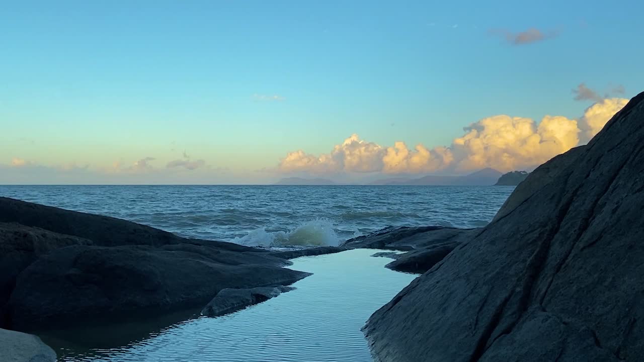 Looking out over the tranquil pacific ocean in North Queensland at dawn, with a crane shot rising over a peaceful rippling rock pool with a stunning view of the orange clouds on the horizon