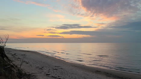 Beautiful-slide-shot-of-a-beach-and-ocean-water-washing-on-the-sand-at-an-orange-sunset---wide-shot