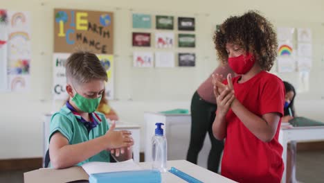 dos niños con máscaras faciales desinfectando sus manos en clase en la escuela