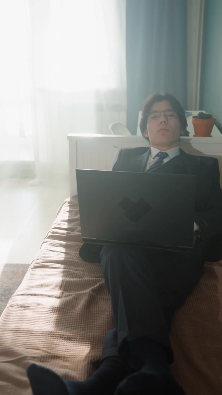 Asian professional working on laptop, crossed legs, suit and tie, morning light through curtain, potted plant on shelf, focused expression, hybrid work vibe, subtle fatigue, home office improvisation