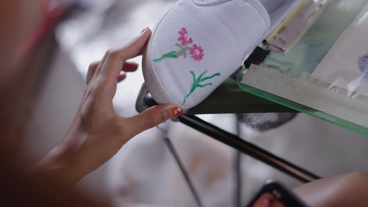 Close-up of hands embroidering a floral design on a white fabric item