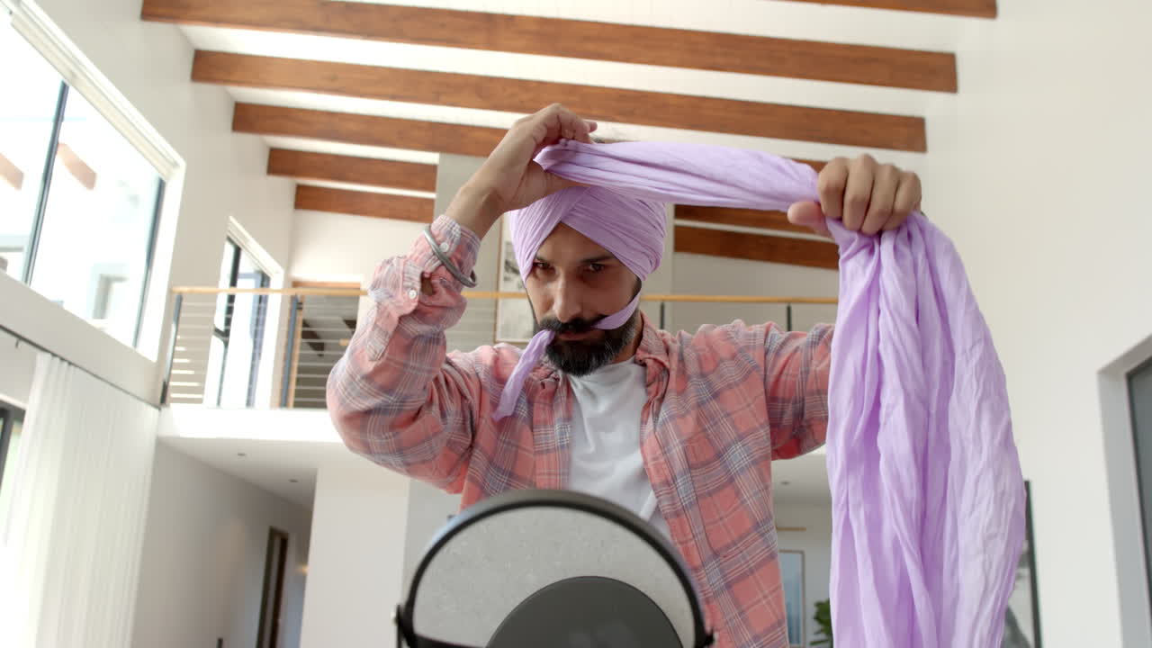 Man wrapping turban in modern home, standing in front of mirror