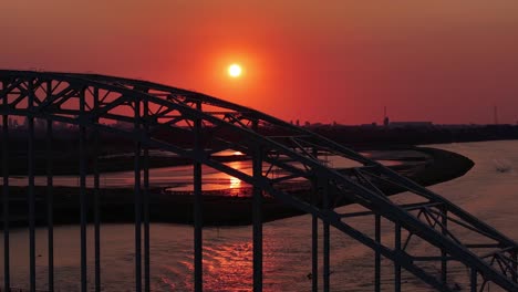 silhouetted arch bridge over the river during sunset with orange sky