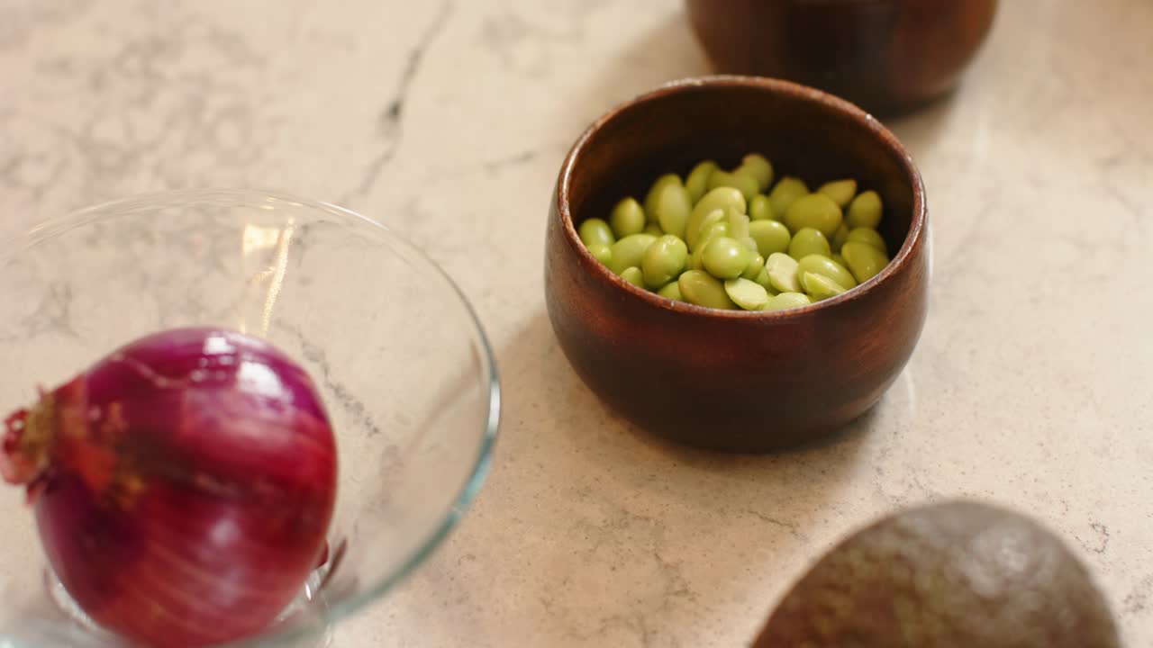Panoramica della telecamera che sposta la cipolla rossa a sinistra, centrando la ciotola di fagioli e mostrando l'avocado condito sul bancone.