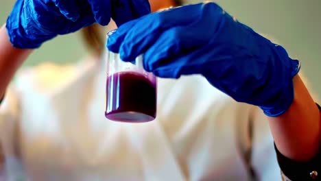 lab technician in blue gloves swirls beaker with purple liquid in scientific experiment