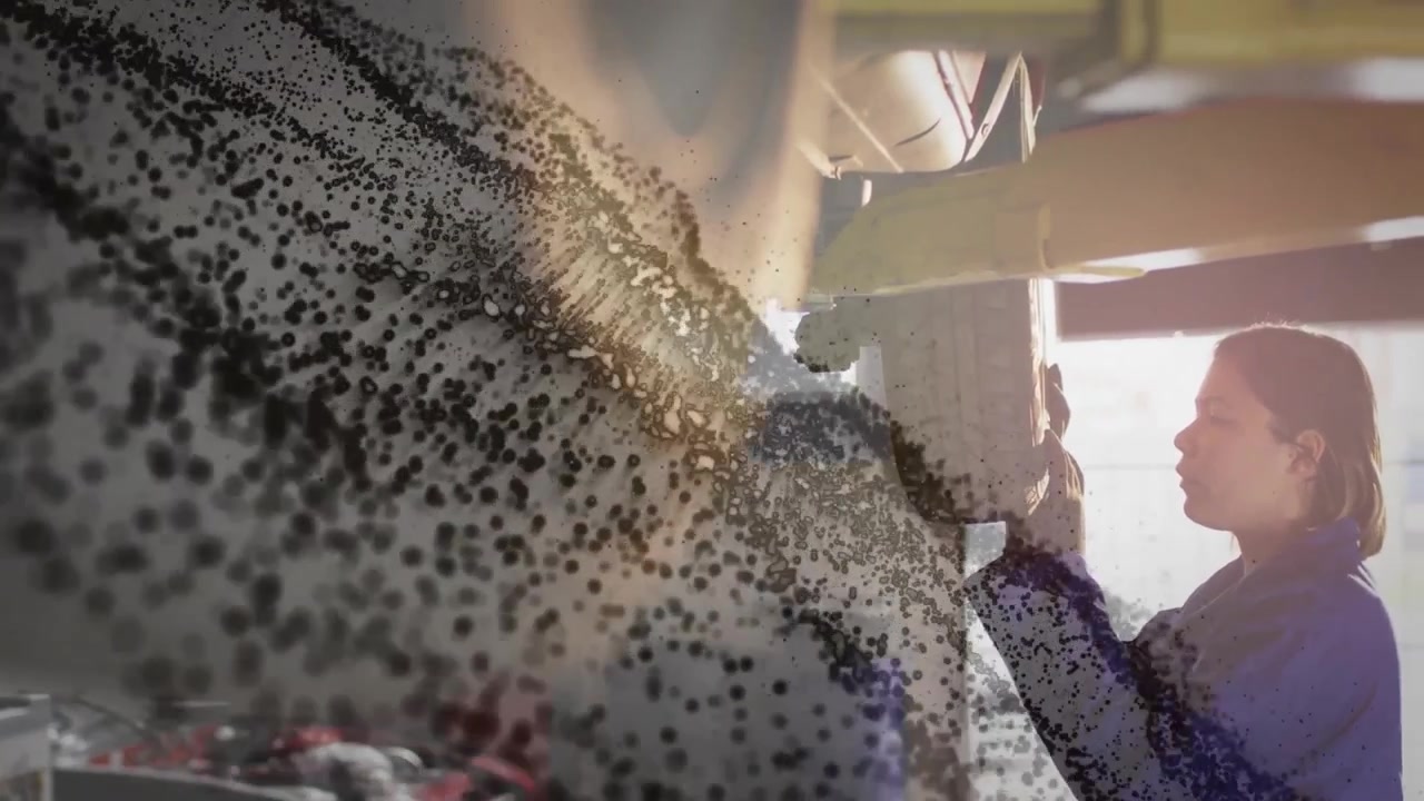 Flusso di particelle che appare da sinistra, rivelando un meccanico che ispeziona il sottoscocca in un'officina automobilistica.