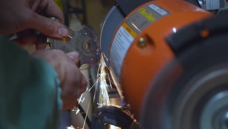 a static high angle shot of a mechanic polishing a welded metallic car piece, with sparks flying down his spinning polishing wheel