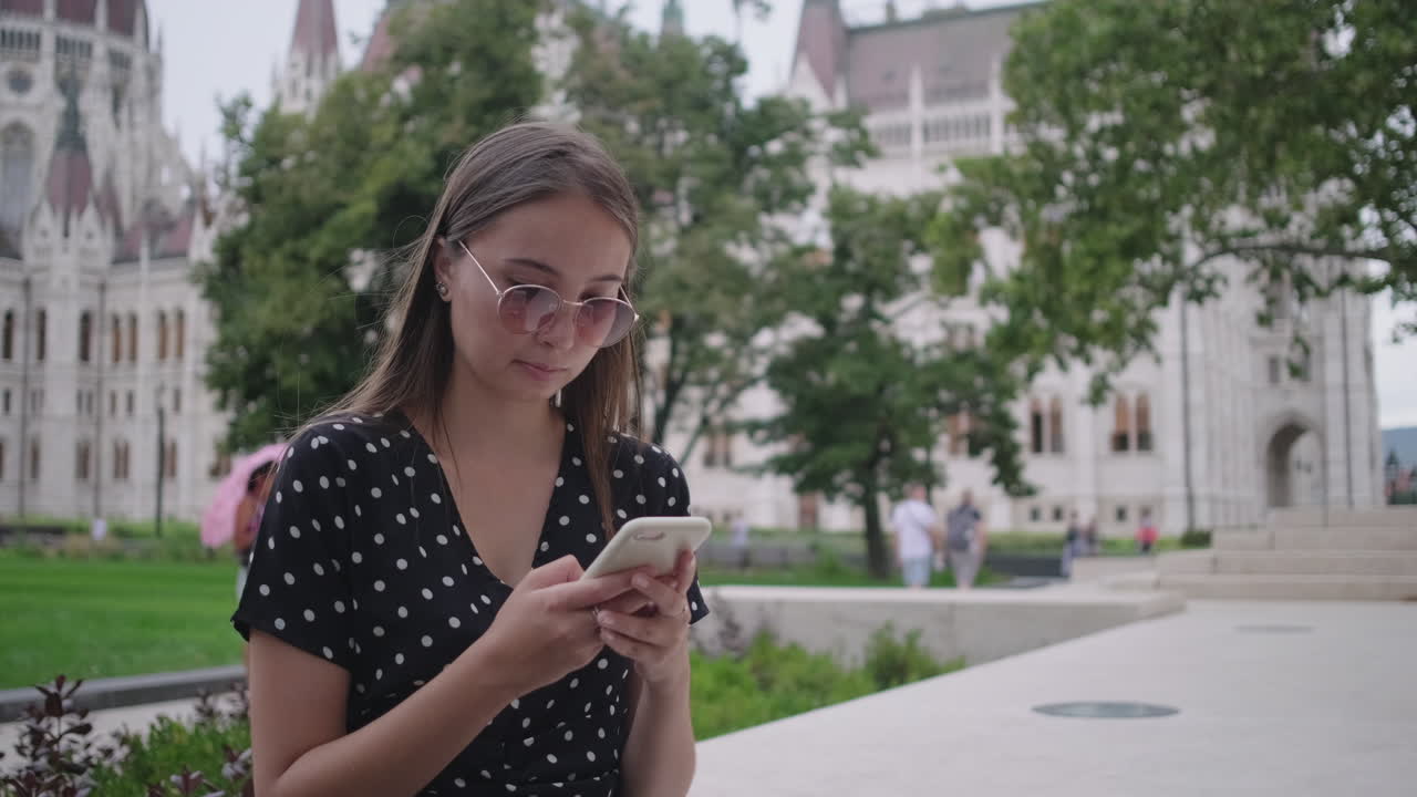 joven usando el teléfono frente al edificio del parlamento húngaro