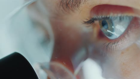eyes of female lab technician in protective glasses looking in microscope